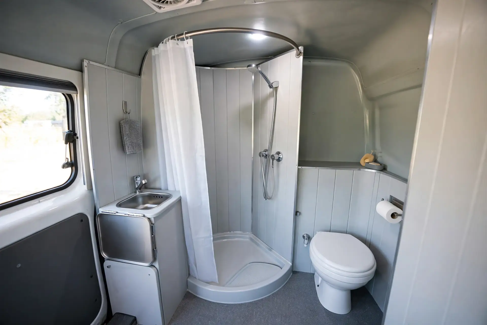 Camper van rear corner wet bath with curved shower curtain, corner tray, toilet and fold-down sink