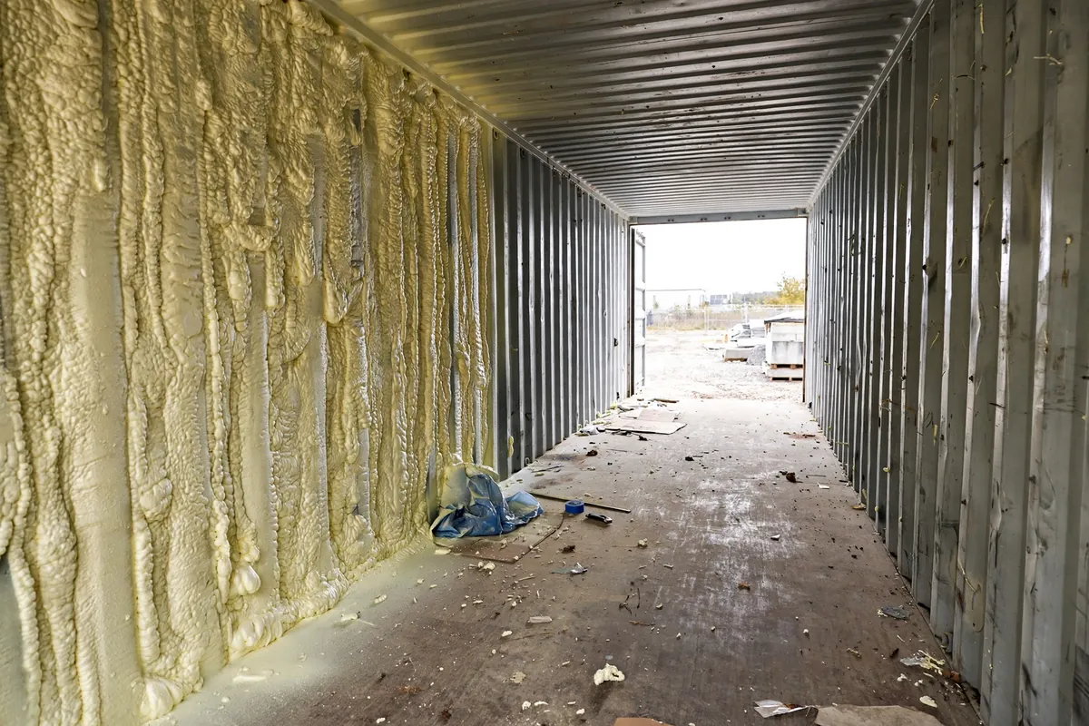 Thick closed-cell spray foam insulation half applied over the corrugated steel wall inside a shipping container